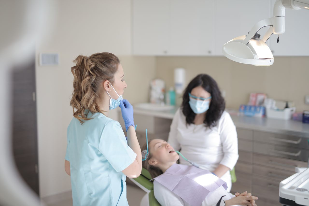 Professional female dentists in mask and gloves curing teeth of patient while working in dental room of modern clinic