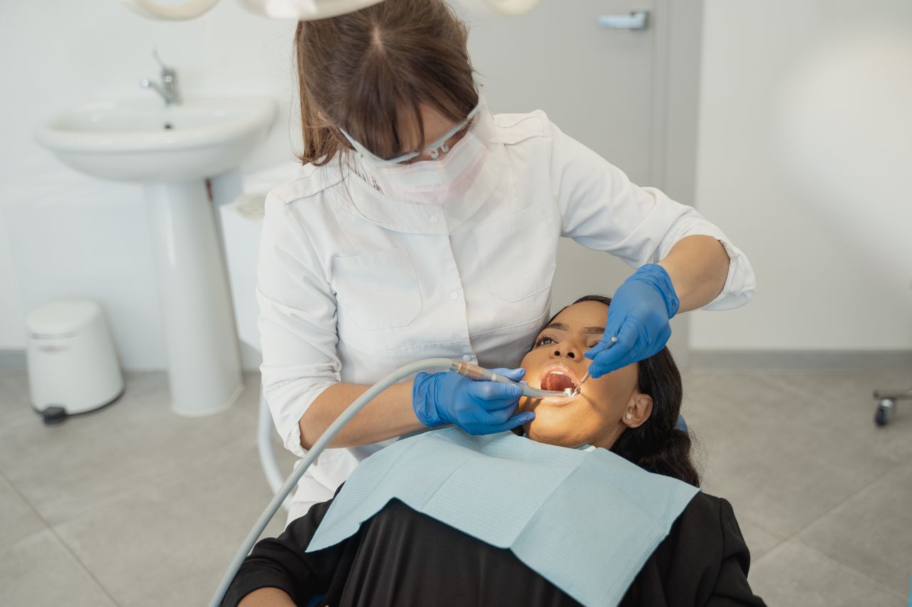 A female dentist wearing a facemask examines a patient's teeth in a dental clinic.